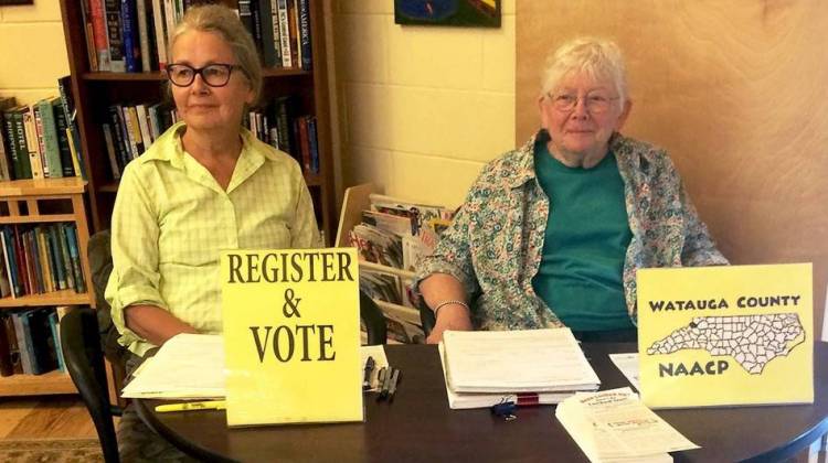 NAACP volunteers Marjorie McKinney (left) and Joan Brannon sit at a booth to register people to vote at the Hospitality House, a community shelter in Boone, N.C.
