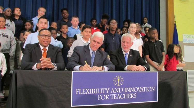 Pence signs House Bill 1009 while IPS Superintendent Lewis Ferebee (left) and Indiana House Education Committee Chairman Robert Behning, R-Indianapolis, and School 88 students look on. - Scott Elliott / Chalkbeat Indiana