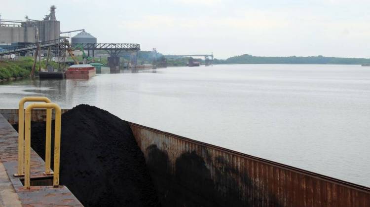 A barge of petcoke, a petroleum byproduct used to make aluminum, waits for offloading at the Port of Indiana-Mt. Vernon, with other barges carrying fertilizer, cement and soybean oil lined up on the Ohio River bank. - Annie Ropeik/IPB News