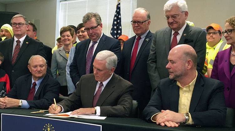 Indiana Gov. Mike Pence signs legislation, surrounded by lawmakers and INDOT employees. - Brandon Smith