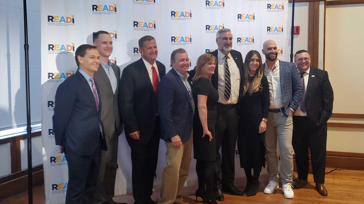 ov. Eric Holcomb stands in the center of a group of state and local officials posing for a photo at the award ceremony for the first round of READI grant funding on Dec. 14, 2021.  - FILE PHOTO: Samantha Horton/IPB News