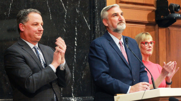 House Speaker Todd Huston (R-Fishers), left and Lt. Gov. Suzanne Crouch, right, stand on either side of Gov. Eric Holcomb, applauding during his 2023 State of the State address. - Brandon Smith/IPB News