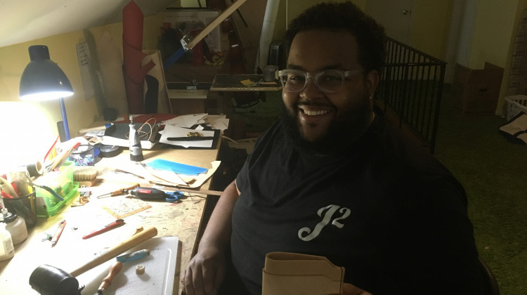 Artist Tracy James creates a leather wallet in his home studio. - WFYI