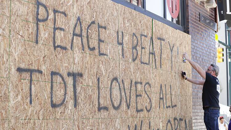 Restaurant owner Michael Cranfill paints a sign on the restaurant's boarded up windows in Indianapolis, Tuesday, June 2, 2020 to honor his friend former Indiana University football player Chris Beaty. Beaty was one of two people fatally shot in Indianapolis during protests over the death of George Floyd. (AP Photo/Michael Conroy)