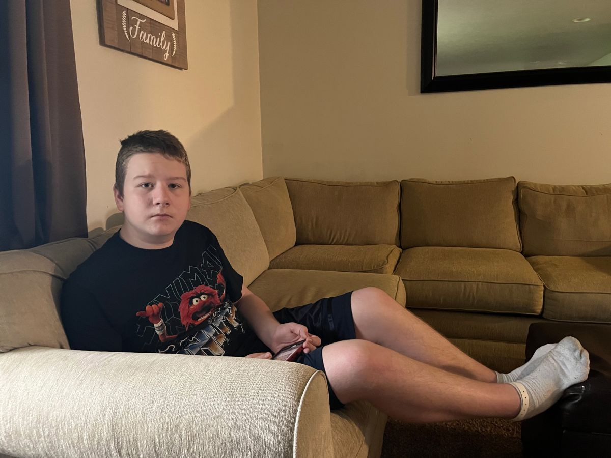 A teenage boy sitting on a sofa. The wall behind has a picture with the word family.