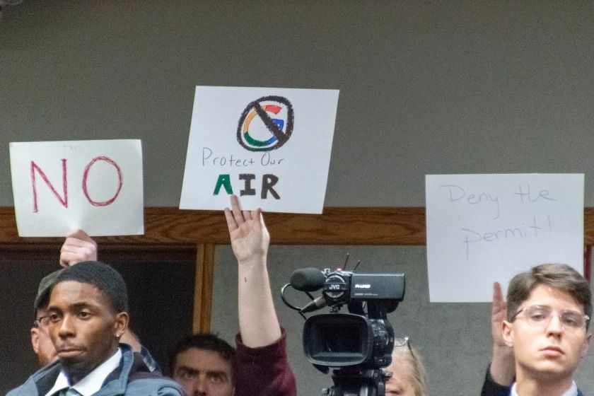 Residents hold sign in the back of the room during the IDEM hearing on November 13. Signs include slogans such as "protect our air," "deny the permit," and more simply "no."