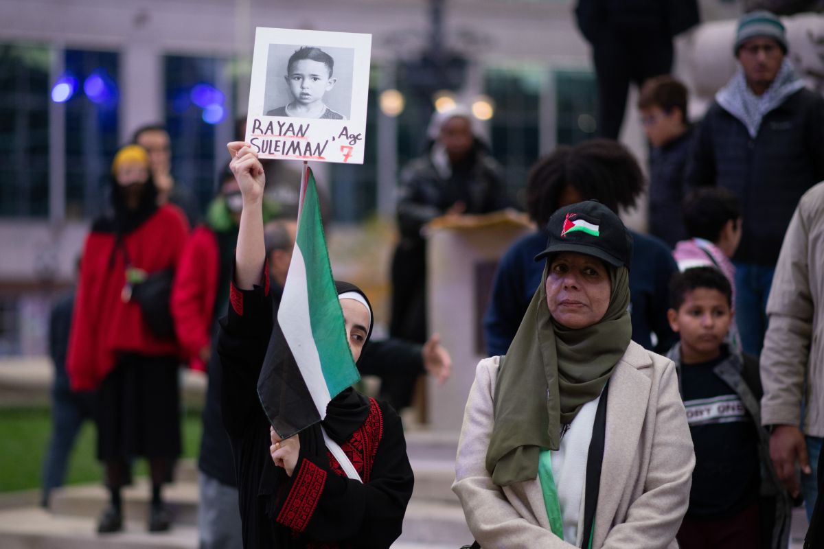 A protester holds up a Palestinian flag and a black and white photo of a boy with the words Rayan Suleiman, age 7