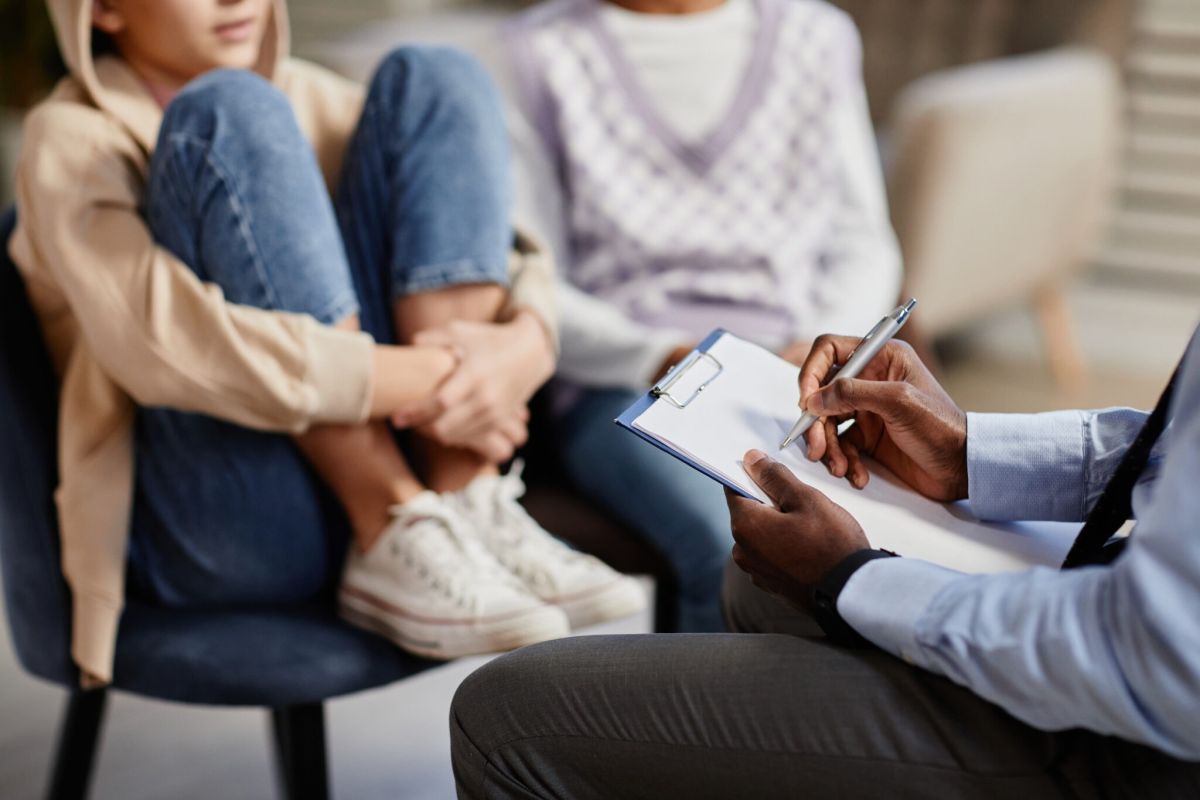 A psychologist takes notes on a clipboard in a therapy session for children.