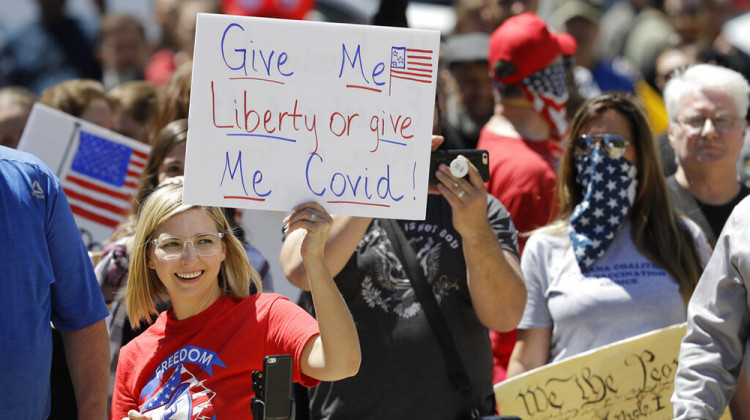 FILE - In this May 1, 2020, file photo, a protester holds a sign during an "Indiana Back to Work" rally at the Statehouse in Indianapolis. Indiana Gov. Eric Holcomb's statewide mask mandate and six months of other coronavirus restrictions has stirred discontent among conservatives, complicating his front-runner campaign against underfunded Democratic challenger Woody Myers. - AP Photo/Darron Cummings, File