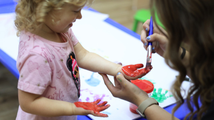 A teacher at The Growing Garden Learning Center paints a student's hand on Wednesday, Oct. 1, 2025 - Zach Bundy/WFYI