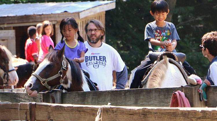 Maddie and Ethan Field, left and right, wait with their father, Travis, for their pony rides to begin at Brown County State Park's Saddle Barn. - Jess Seabolt, TheStatehouseFile.com