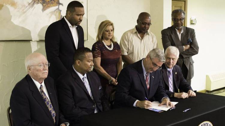 Gov. Eric Holcomb signs HB 1344 as Rep. Earl Harris, Jr., Mayor Anthony Copeland, Sen. Lonnie Randolph, and others watch. - Nick Janzen/IPB