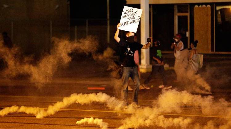A protester stands in the street after police fired tear gas to disperse a crowd Sunday, Aug. 17, 2014, during a protest for Michael Brown, who was killed by a police officer last Saturday in Ferguson, Mo. - AP Photo/Charlie Riedel