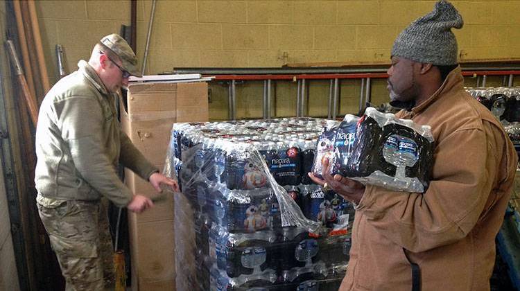 Staff Sgt. William Phillips, with the Michigan National Guard, assists a resident at a water distribution center Wednesday, Jan. 13, 2016, at a fire station in Flint, Mich. - AP Photo/Mike Householder