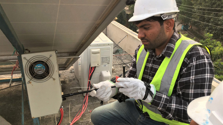 A man installing solar panels on a roof. - U.S. Agency for International Development - Pakistan/Wikimedia Commons