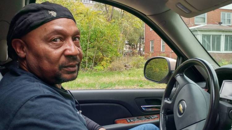 Mike Mitchell sits in front of what was once his childhood home, which is now just weeds and wood scraps. - Annie Ropeik/Indiana Public Broadcasting