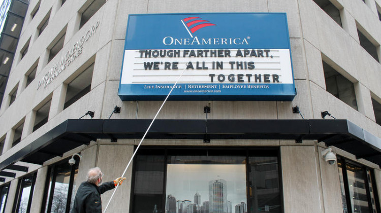 A man adjusts the One America sign in downtown Indianapolis. It usually displays a pun, but the message shortly before the governor's address reads: 'Although farther apart, we're all in this together.' - Lauren Chapman/IPB News