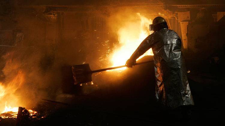 A worker throws insulation on top of molten iron and slag as it flows from a blast furnace at ArcelorMittal's mill at Burns Harbor, Ind. in June 2006. - AP Photo/M. Spencer Green, File