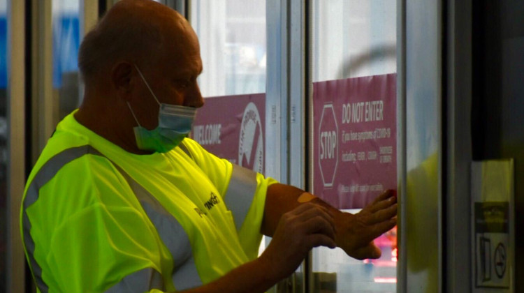 A worker at a Pilot Travel Center gas station in Greenfield, Indiana puts a sticker on the door telling patrons not to enter if they feel symptoms associated with COVID-19.  - Justin Hicks/IPB News